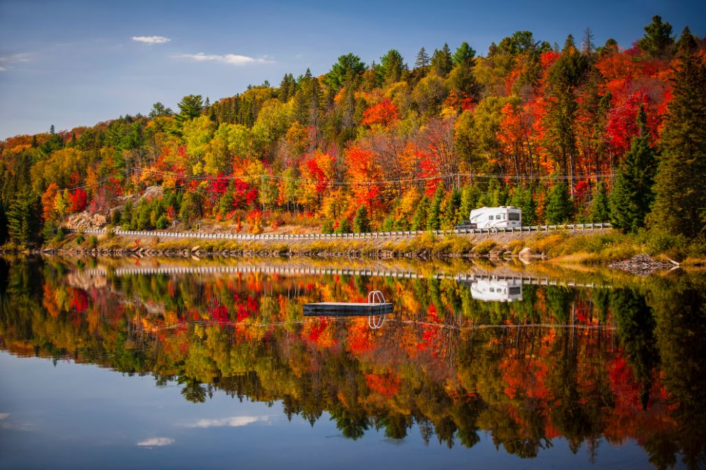 Herbstwald mit buntem Herbstlaub und Highway 60, der sich im Lake of Two Rivers spiegelt.  Algonquin Park, Ontario, Kanada.